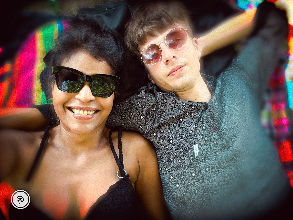 Natalie and Danny wearing sunglasses, lying together on a colourful blanket.