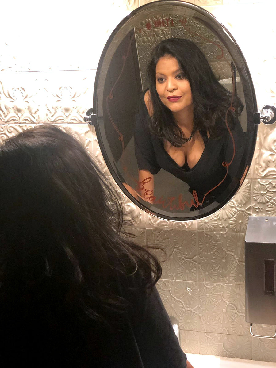 Natalie looking into an oval mirror surrounded by an embossed metallic wall.